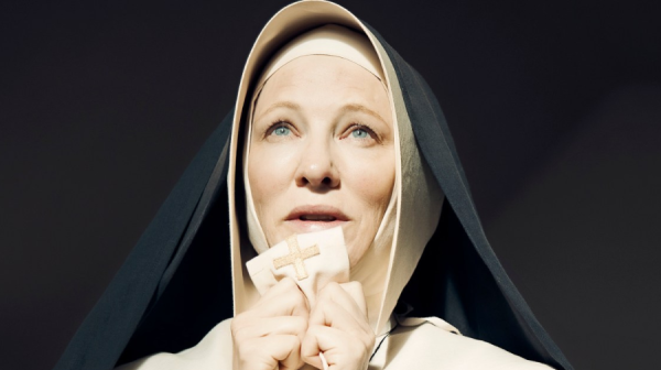 Cate Blanchett in a Nun's habit and wimple, clutches a surplice with a crucifix sewed onto it, to her mouth 