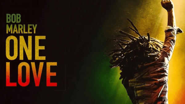 A black man with dreads stands with his back to the camera, right hand raised in a fist of protest, against a backdrop of the colours of the Jamaican flag. The words One Love Bob Marley are on the far left 