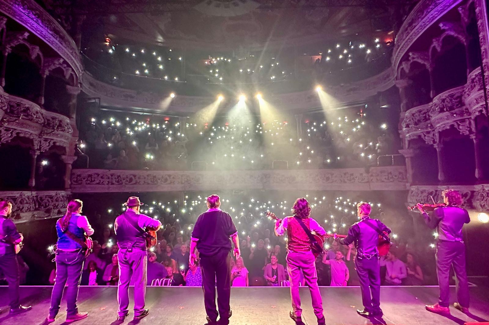 image of 7 people stood on stage looking out to a full theatre auditorium