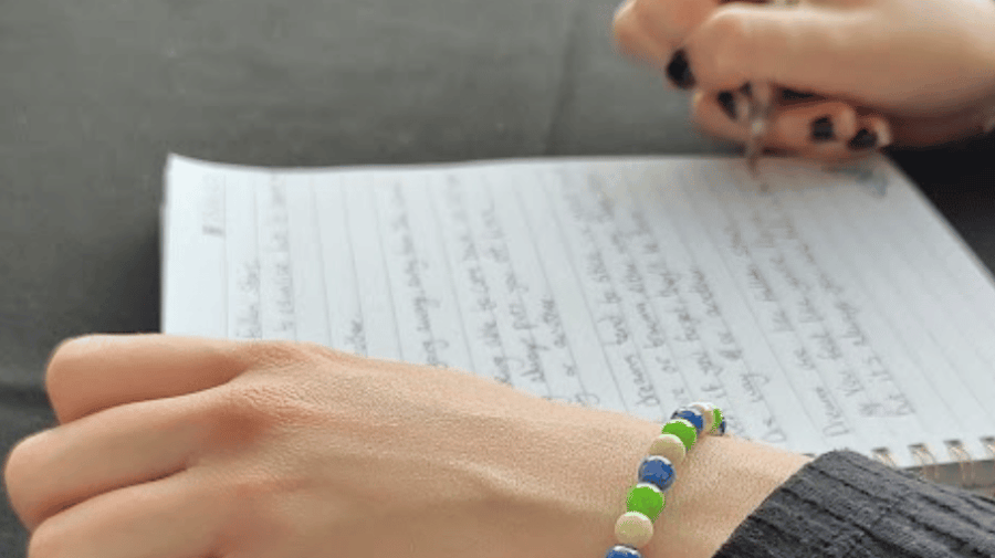 a pair of hands holding a pen and a sheet of paper with writing on it 