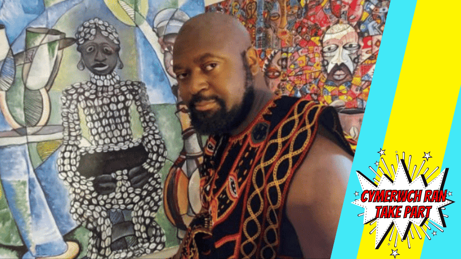 a black man with a shaved head wearing traditional african clothes stands in front of colourful African artwork 