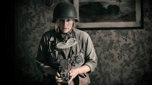 Kate Winslet as Lee. Against a dark paisley wallpaper, in Army fatigues and tin helmet, focusing a camera