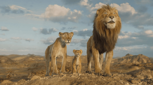 a male Lion, a Lioness and their cub, stand on  the savannah, looking over their land. Behind them, a blue sky with fluffy white clouds 