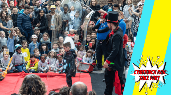 a crowd of people watch a man in a top hat put a giant bubble around a child 