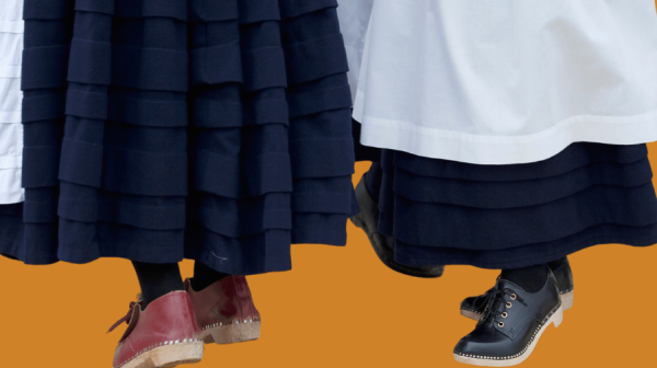 an orange background and two traditionally dressed Welsh cloggers, wearing long skirts